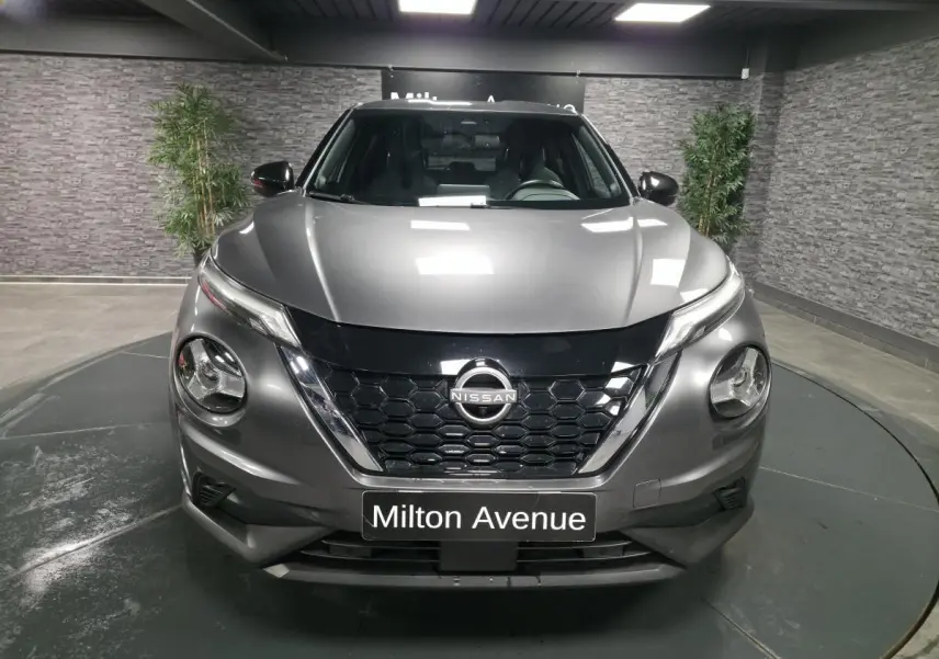 Vue avant d'un Nissan Juke gris métallisé 2024 avec calandre noire et phares LED ronds dans un showroom.