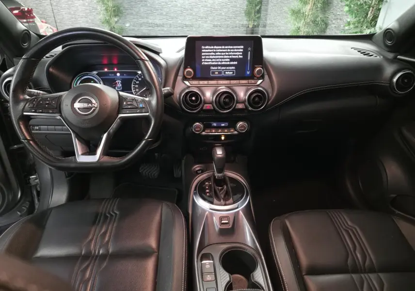 Vue intérieure avant du Nissan Juke 2024 gris, avec volant cuir, écran tactile central et sellerie cuir noire.