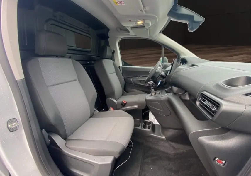 Vue intérieure côté conducteur du Peugeot Partner blanc 2024, montrant les sièges avant gris et le tableau de bord moderne.