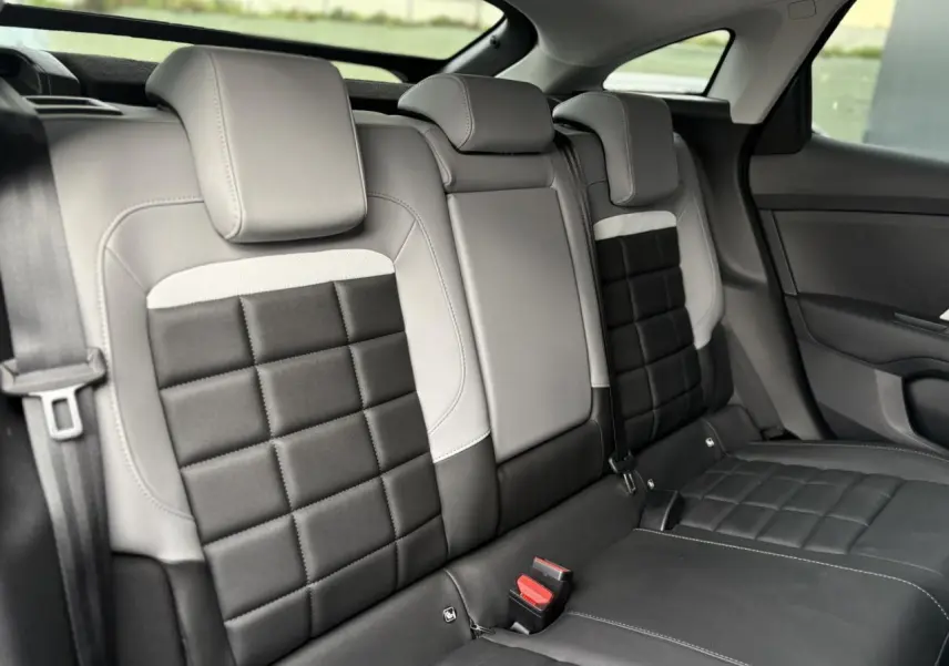 Vue intérieure de la banquette arrière de la Citroën C4 Hybrid 2025, avec sièges bicolores gris clair et noir matelassé.