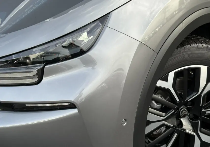 Gros plan sur l'avant droit gris Mercury du Citroën C4 Hybrid 2025, mettant en valeur le phare LED et la jante alliage 18 pouces.
