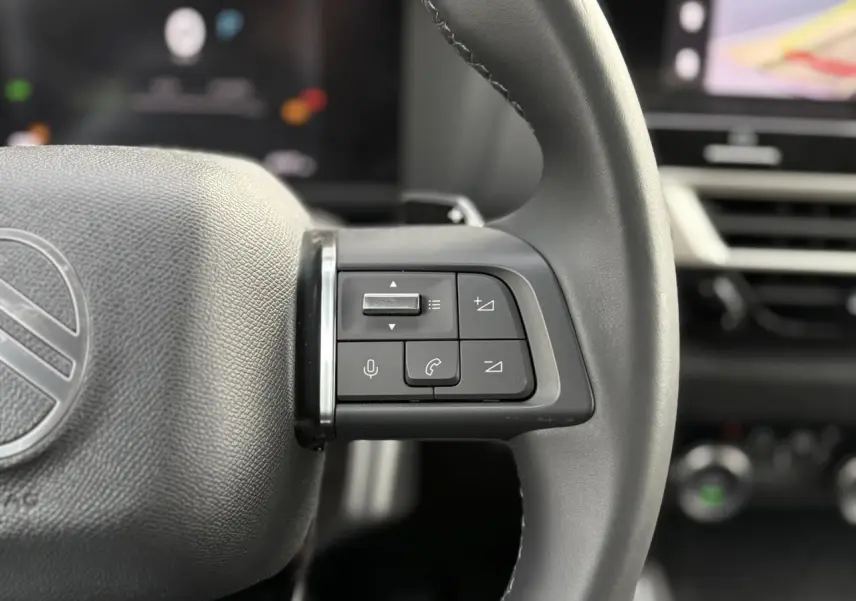 Gros plan sur les commandes du volant à droite du Citroën C4 Hybrid 2025, intérieur noir avec écran tactile en arrière-plan.