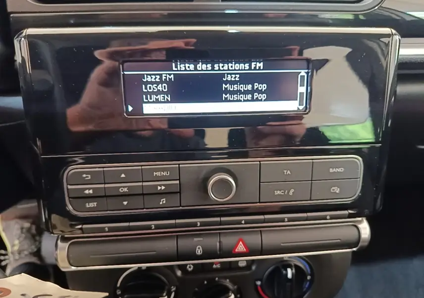 Vue rapprochée du tableau de bord noir de la Citroën C3 avec écran radio affichant la liste des stations FM.