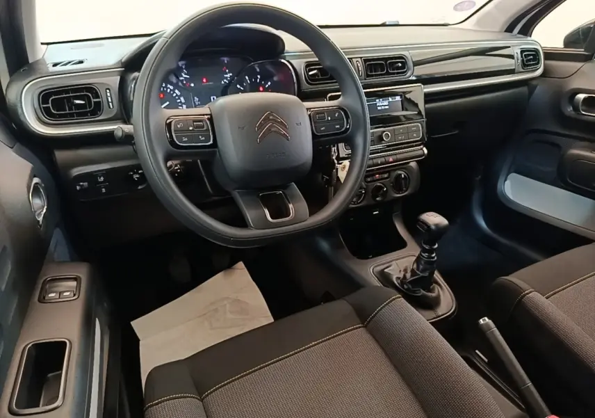 Vue intérieure avant centrée sur le volant multifonctions et la console centrale d'une Citroën C3 blanche de 2019 avec boîte manuelle.