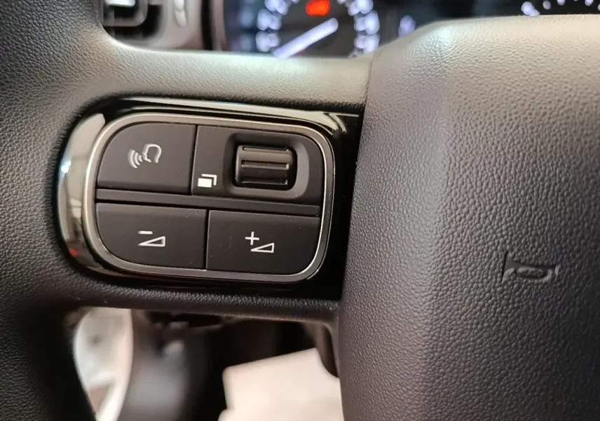 Gros plan sur les commandes gauche du volant noir d'une Citroën C3 blanche, avec boutons de volume et appel mains libres.