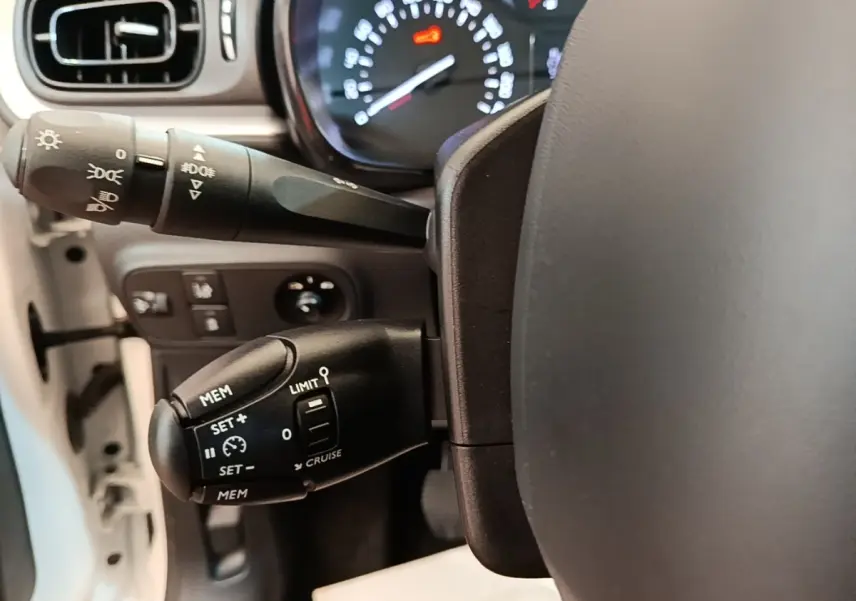 Gros plan sur la colonne de direction et commandes du régulateur de vitesse d'une Citroën C3 blanche, intérieur clair.