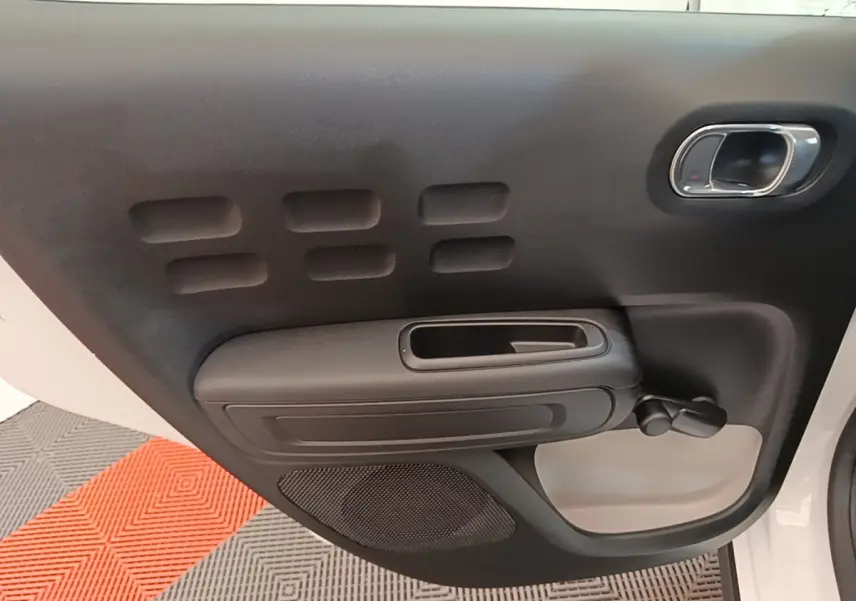 Vue rapprochée de la porte intérieure côté droit de la Citroën C3 blanche, avec poignée et commande de vitre manuelle.