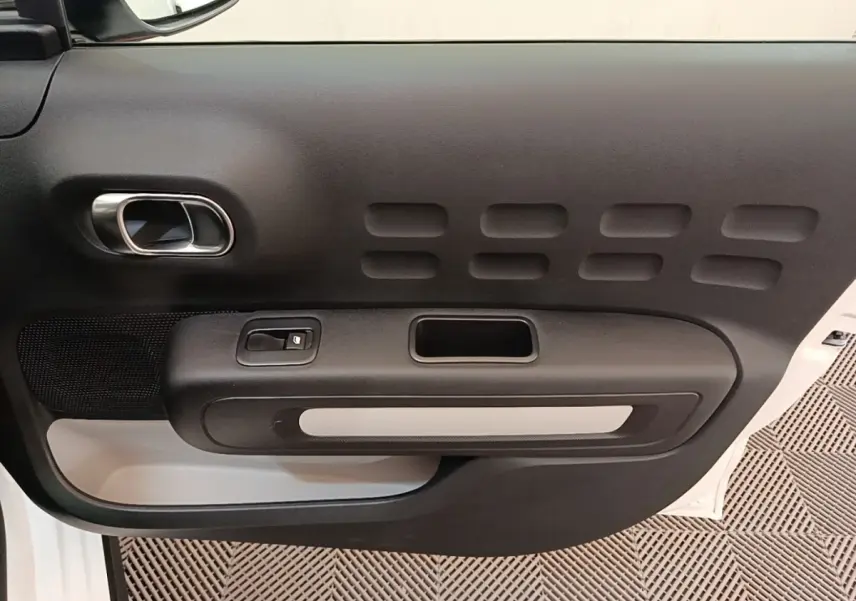 Vue rapprochée de la porte intérieure côté gauche d'une Citroën C3 blanche, avec poignée et commande de vitre.