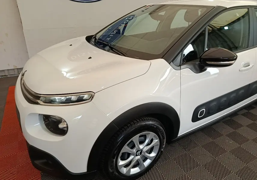 Vue 3/4 avant droit d'une Citroën C3 blanche avec protections latérales noires et jantes alliage argentées.