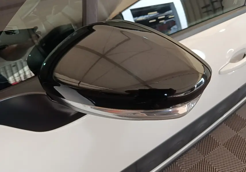 Gros plan sur le rétroviseur droit noir brillant d'une Citroën C3 blanche, avec poignée de porte visible en arrière-plan.