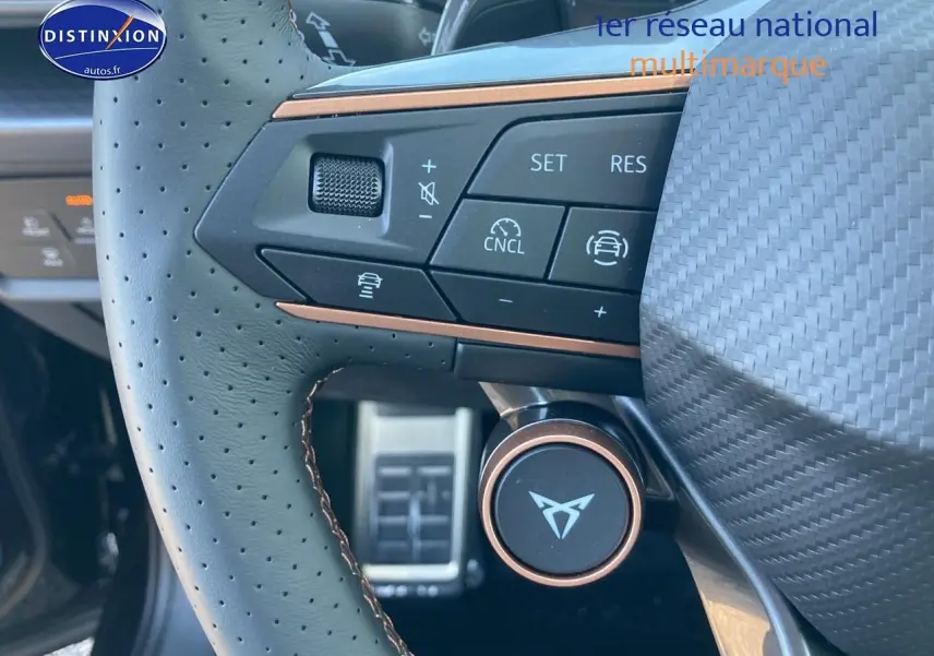 Gros plan sur le volant cuir perforé noir avec commandes multifonctions et logo CUPRA au centre.