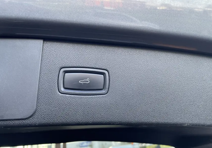 Bouton d'ouverture électrique du hayon sur la garniture intérieure du coffre d'un Porsche Cayenne gris Kerguelen 2018.