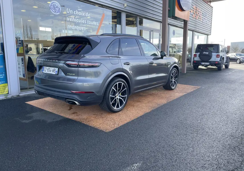 Vue 3/4 arrière droite d'un Porsche Cayenne E-Hybrid gris Kerguelen 2018 avec jantes noires et détails verts e-hybrid.
