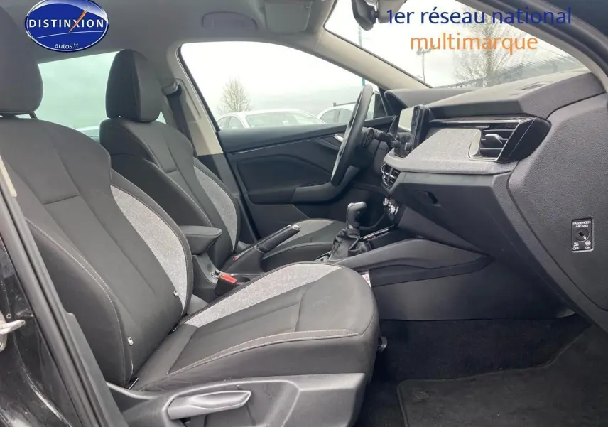 Vue intérieure côté gauche du poste de conduite du Skoda Kamiq noir 2025, avec sièges tissu bicolore et tableau de bord moderne.