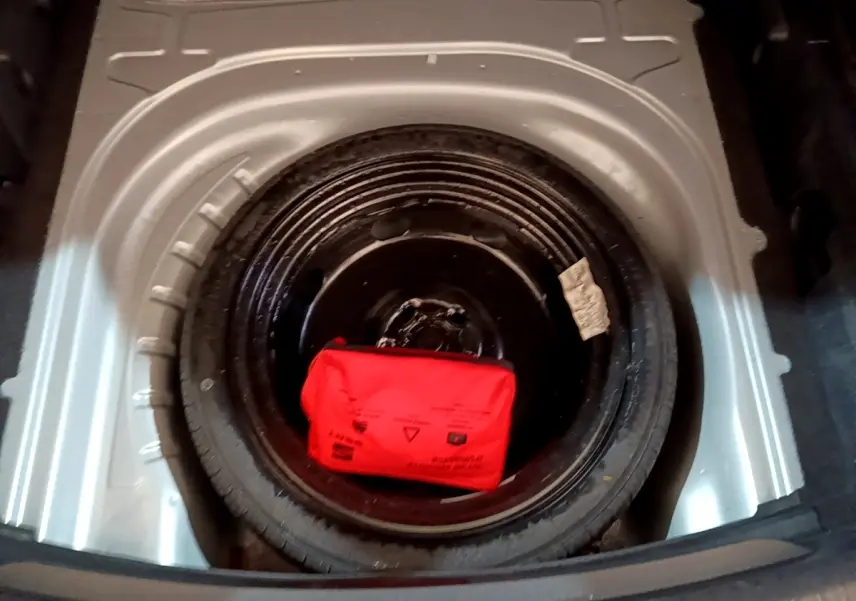 Gros plan sur la roue de secours galette noire dans le coffre d’une SEAT LEON gris foncé, avec trousse de secours rouge.