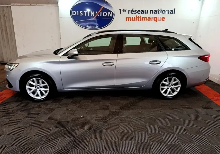 Vue de profil côté gauche d'une SEAT Leon break gris clair stationnée en intérieur sur sol noir et rouge.