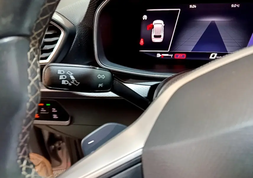 Gros plan sur le tableau de bord numérique et la commande de clignotants du SEAT Leon gris foncé, intérieur moderne.