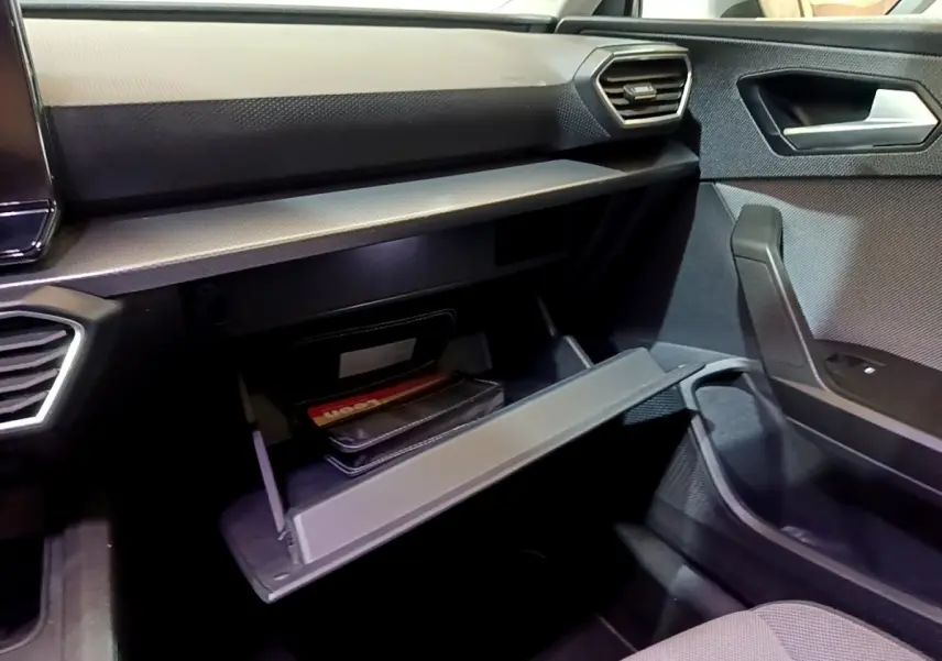 Intérieur côté passager du SEAT Leon gris foncé 2022, avec boîte à gants ouverte et tableau de bord moderne.