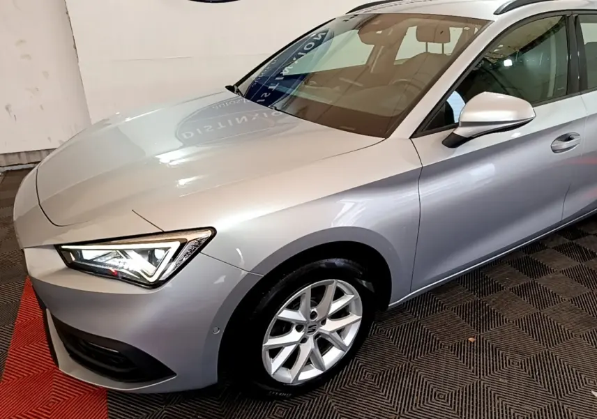 Vue 3/4 avant droit d'une SEAT Leon gris clair avec phares LED allumés dans un showroom.