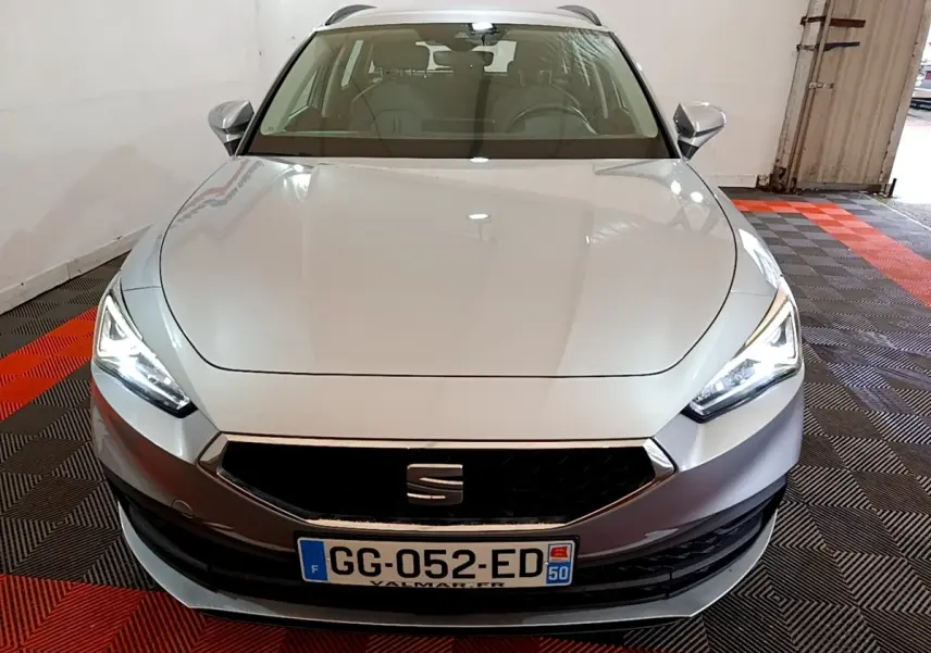 Vue avant d'une SEAT Leon gris foncé avec phares LED allumés, garée sur un sol à motifs rouges et noirs.
