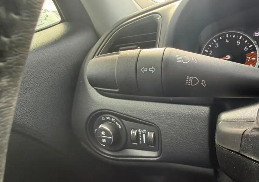 Gros plan sur la commande des phares et clignotants à gauche du volant dans l’habitacle noir du Jeep Renegade bleu 2023.