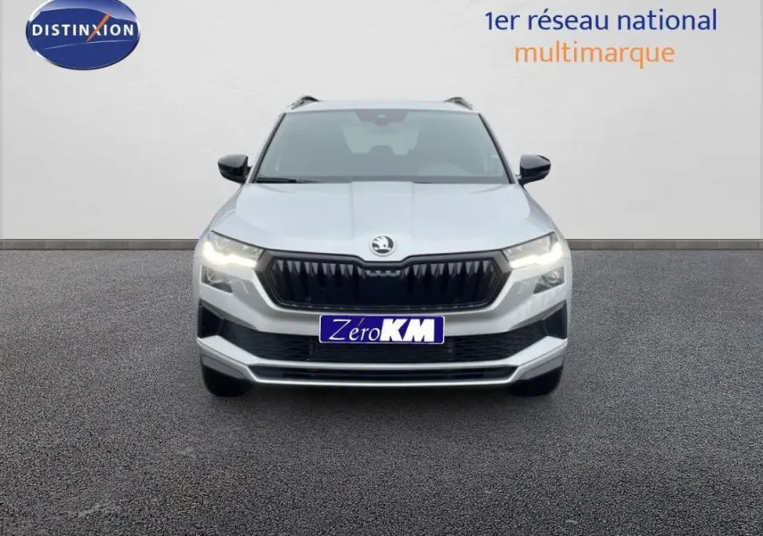 Vue de face du SUV SKODA KAROQ argent 2025 avec calandre noire et phares allumés sur fond neutre.