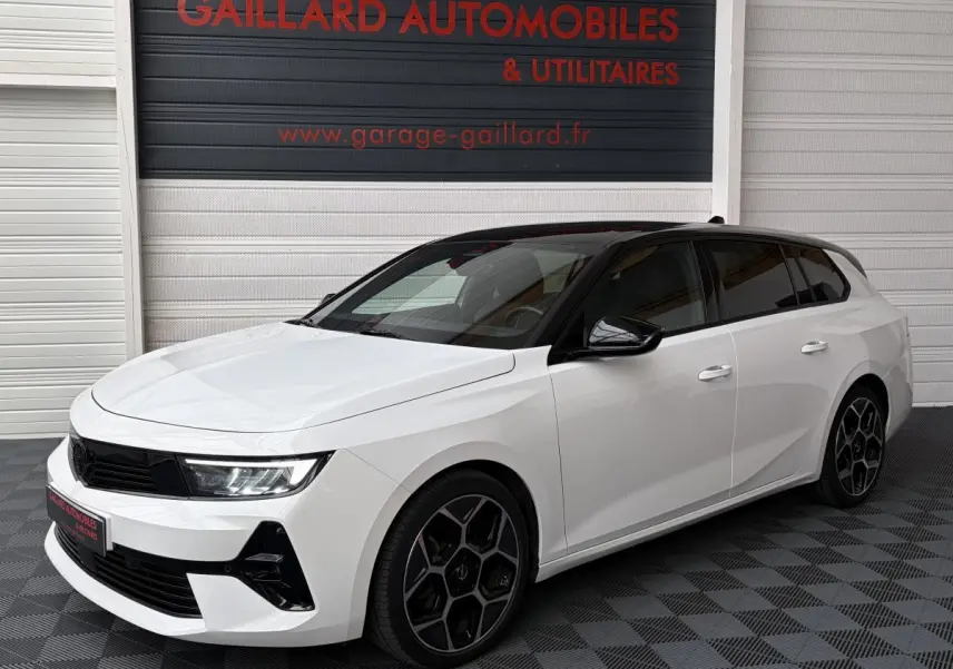 Opel Astra 2024 blanche vue 3/4 avant droit avec toit noir et jantes noires au showroom.