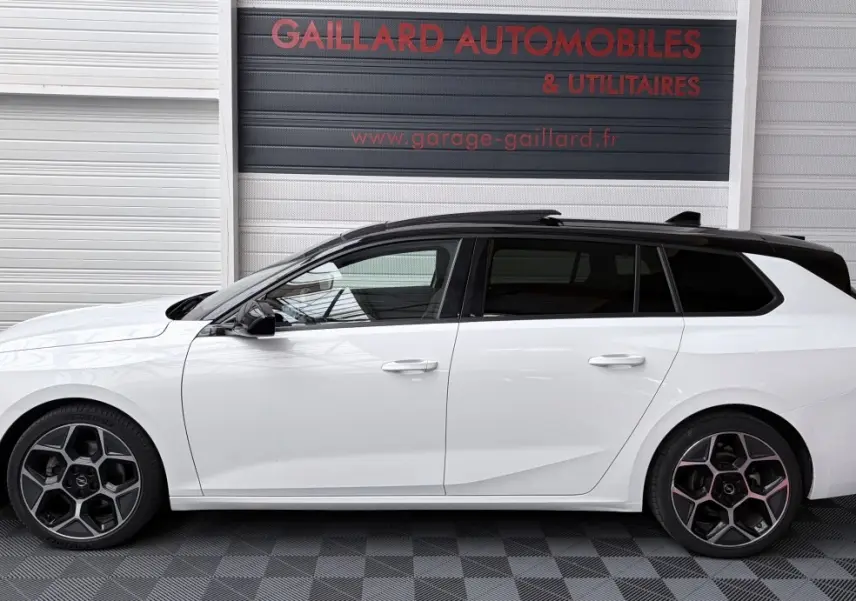 Vue latérale gauche d'une Opel Astra blanche avec toit noir et jantes alliage au design hexagonal.