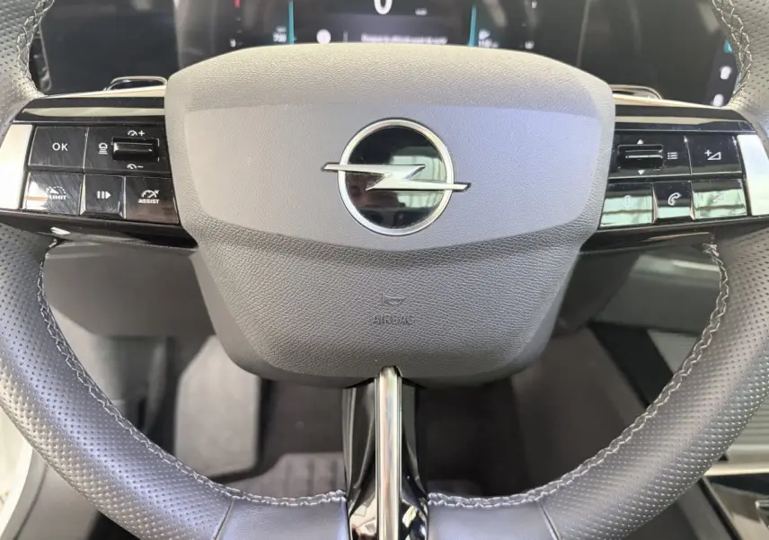 Gros plan sur le volant cuir noir perforé de l’Opel Astra 2024 avec commandes multifonctions et logo central chrome.