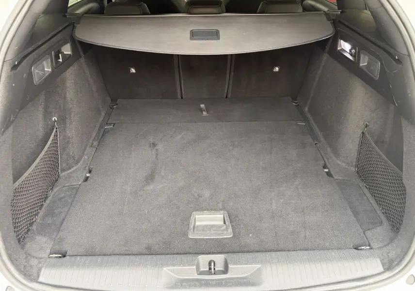 Coffre spacieux de l’Opel Astra blanc, vue arrière ouverte avec cache-bagages et filet latéral.