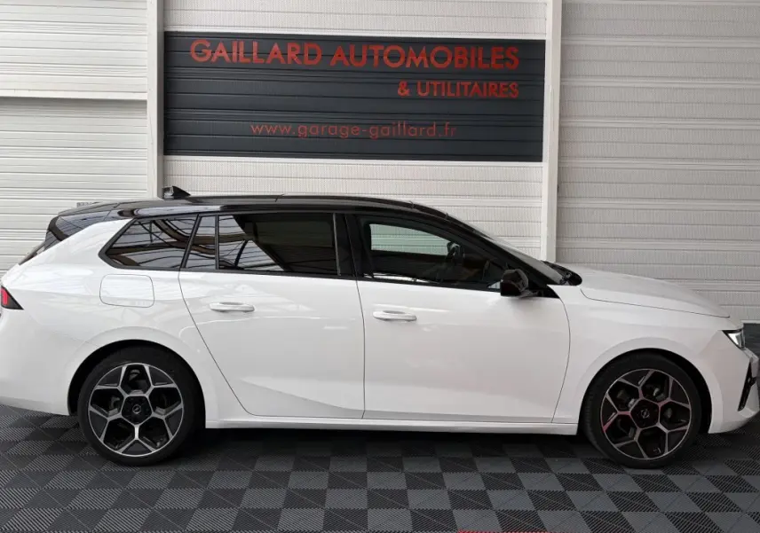 Vue latérale droite d'une Opel Astra blanche avec toit ouvrant noir, jantes alliage et vitres teintées.