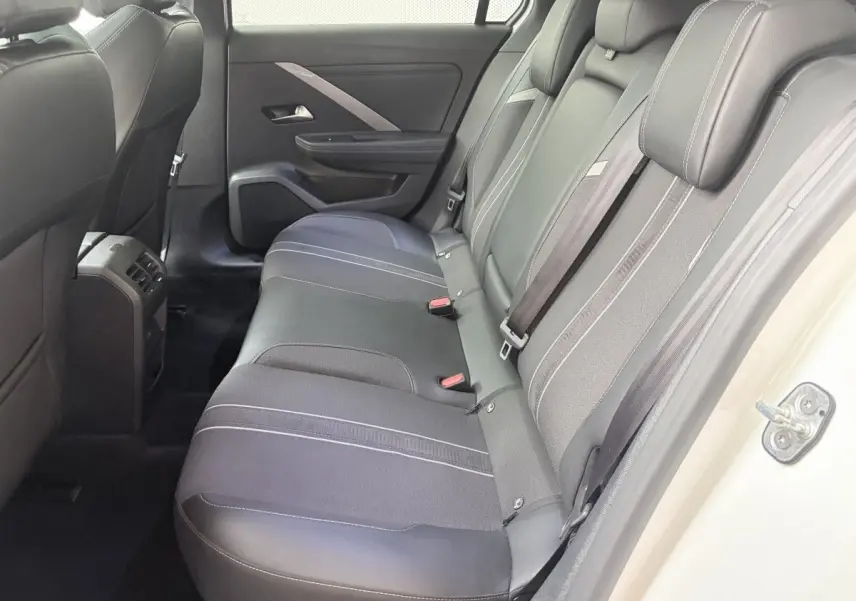 Vue intérieure côté droit sur la banquette arrière noire de l’Opel Astra blanche avec porte ouverte.