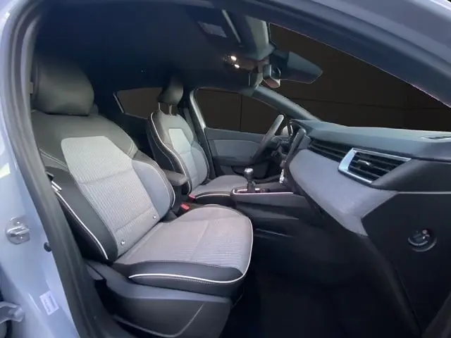 Vue intérieure côté conducteur de la Renault Clio Techno TCe 90 gris clair, montrant les sièges et le tableau de bord moderne.