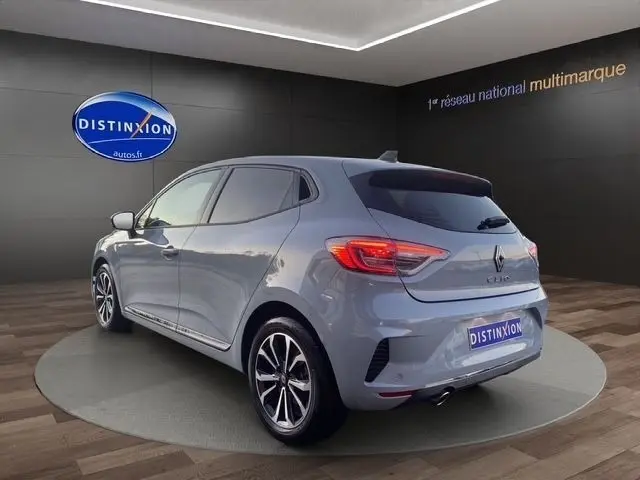 Vue 3/4 arrière droite d'une Renault Clio gris clair 2025 en showroom avec jantes alliage et feux LED distinctifs.