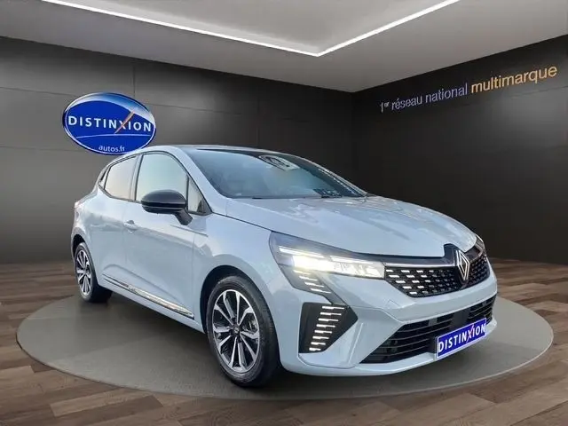 Renault Clio Techno TCe 90 gris clair vue 3/4 avant avec phares LED allumés dans un showroom.
