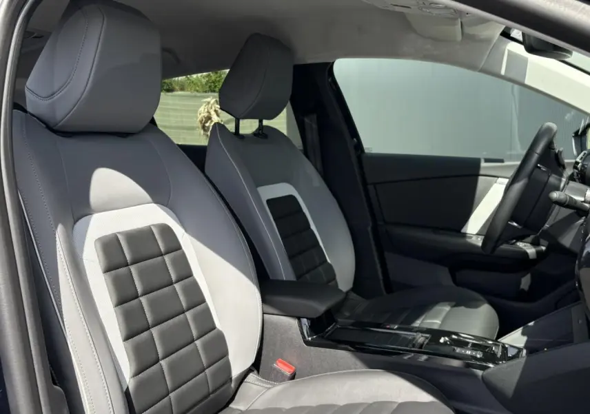 Vue intérieure côté gauche des sièges avant gris clair et noir avec accoudoir central et volant de la Citroën C4 Hybrid 2025.