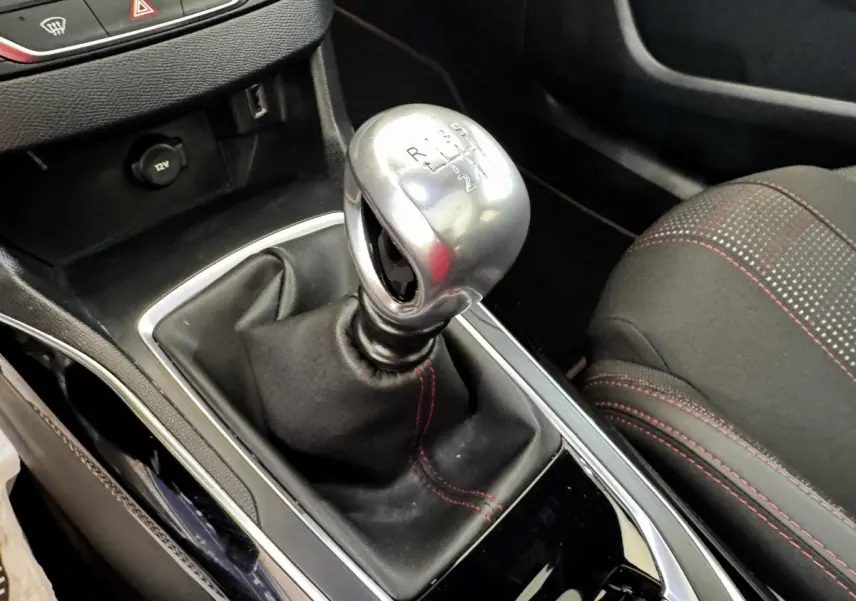 Gros plan sur le levier de vitesse manuel chromé et la console noire avec surpiqûres rouges du siège avant droit de la Peugeot 308.