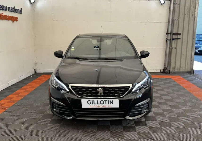Vue avant frontale d'une Peugeot 308 noire avec calandre chromée et feux LED allumés dans un garage.