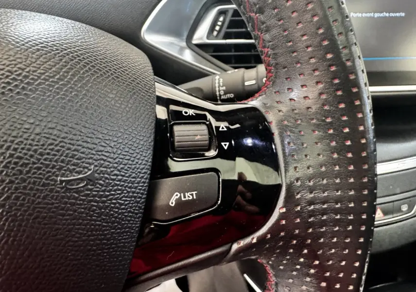 Gros plan sur le volant cuir noir perforé avec surpiqûres rouges du Peugeot 308 GT Line, commandes intégrées visibles.