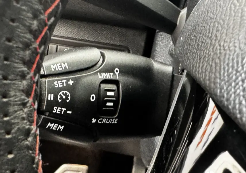 Gros plan sur la commande de régulateur de vitesse noire, avec volant cuir noir et surpiqûres rouges visible, Peugeot 308.