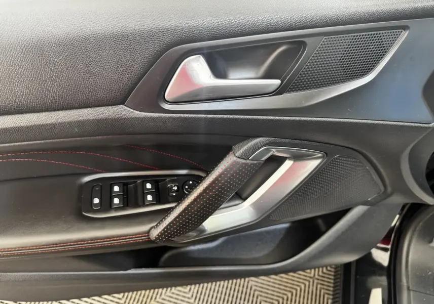 Gros plan sur la porte intérieure côté conducteur noire avec surpiqûres rouges et commandes des vitres du Peugeot 308 GT Line.