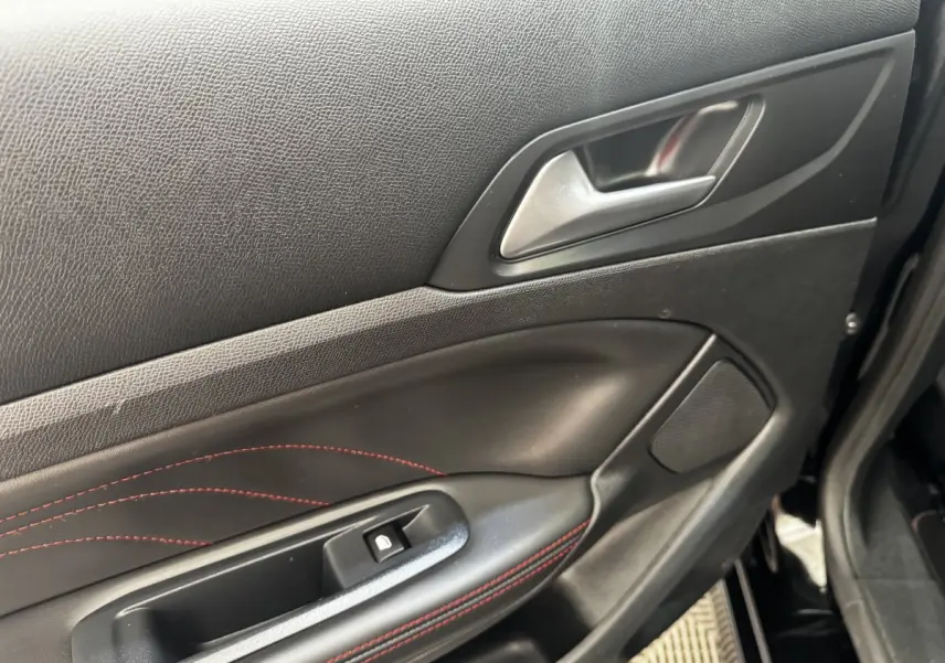Détail de la porte avant gauche noire de la Peugeot 308 GT Line avec surpiqûres rouges et poignée argentée.