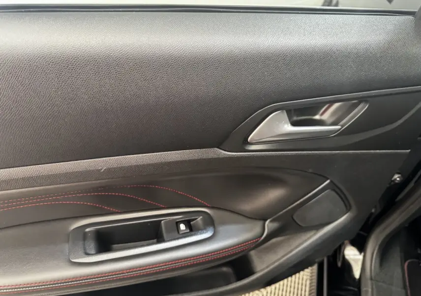 Intérieur côté gauche de la porte avant d’une Peugeot 308 noire, avec surpiqûres rouges et poignée argentée.