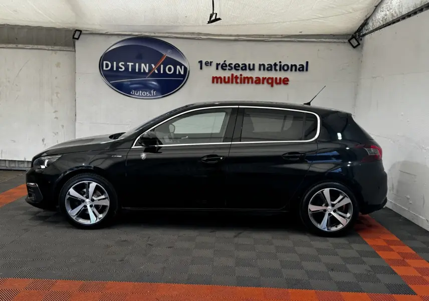Vue de profil côté gauche d'une Peugeot 308 noire GT Line 2018 dans un showroom avec sol à damier gris et orange.