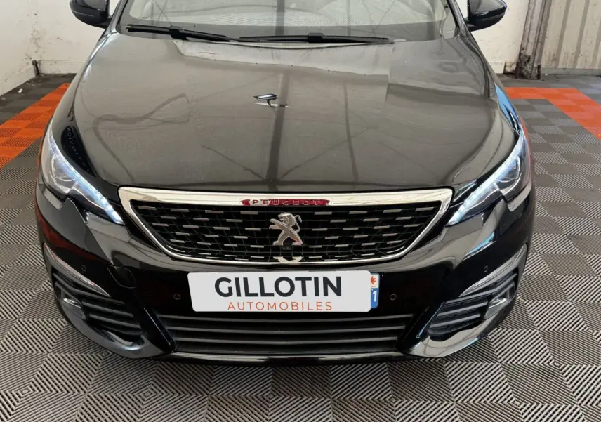Vue avant rapprochée de la Peugeot 308 noire avec calandre chromée et feux LED allumés sur sol damier.