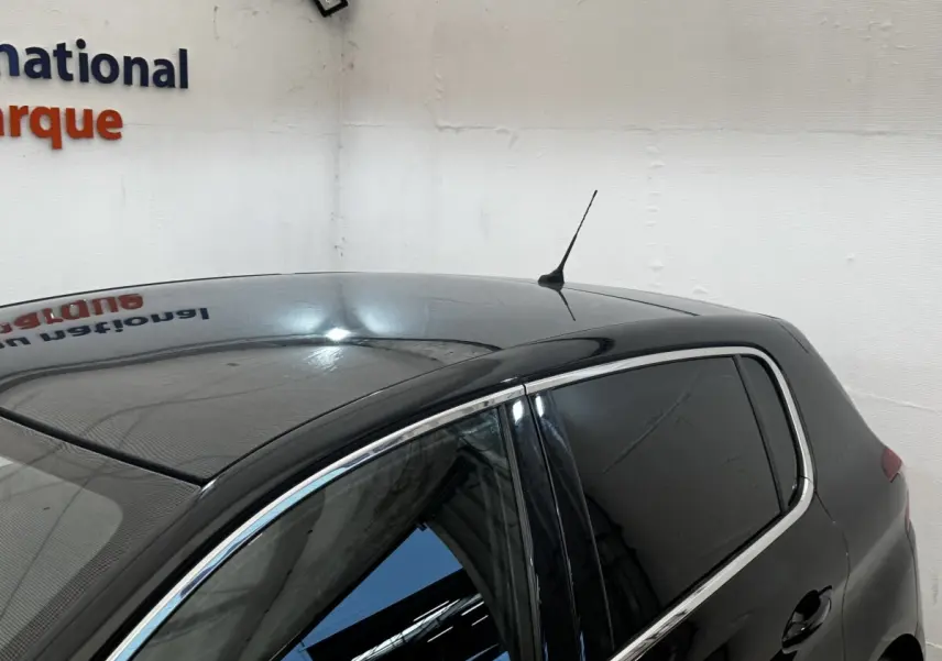 Vue 3/4 arrière droite d'une Peugeot 308 noire avec vitres teintées et antenne de toit visible.