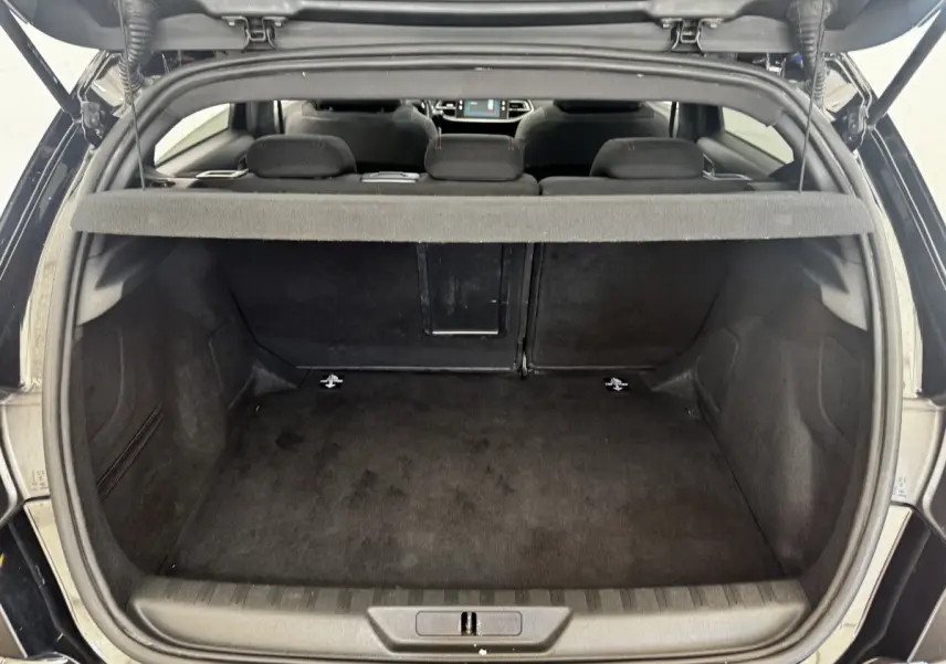 Vue arrière du coffre ouvert d'une Peugeot 308 noire, montrant l'espace de chargement et la banquette arrière rabattue partiellement.
