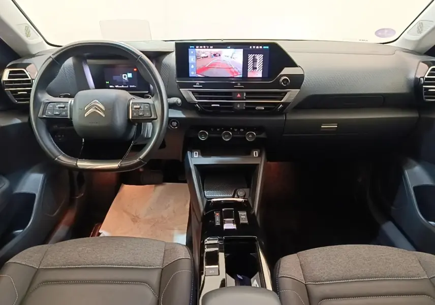 Vue intérieure frontale du tableau de bord et volant cuir noir du Citroën C4 X 2023 avec écran tactile central allumé.