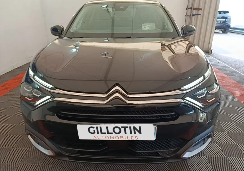 Vue frontale d'une Citroën C4 X noire 2023 avec phares LED et calandre chromée dans un garage.