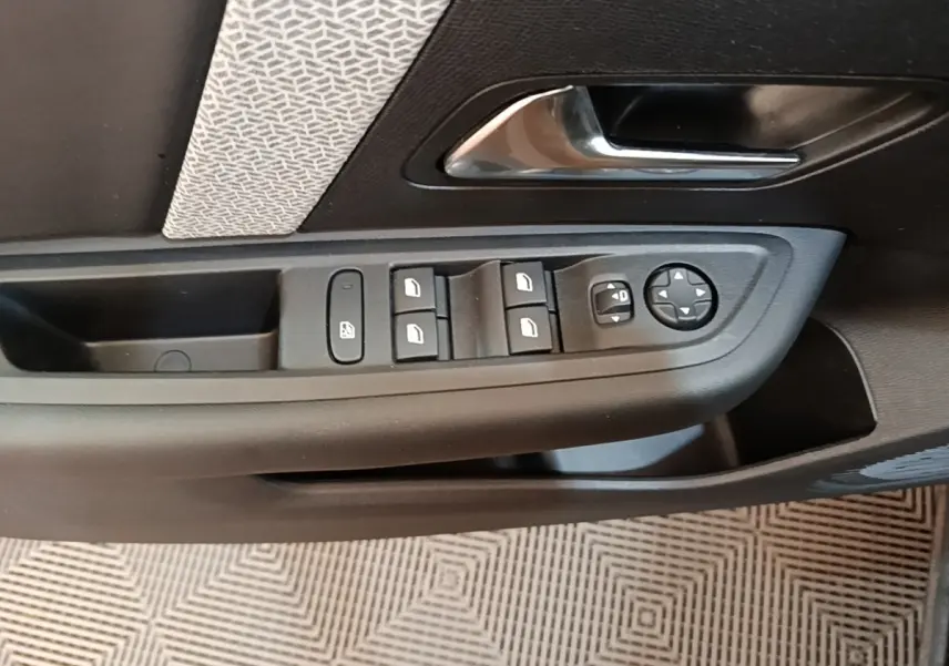 Gros plan sur la commande des vitres et rétroviseurs côté conducteur d'une Citroën C4 X noire, intérieur tissu gris.